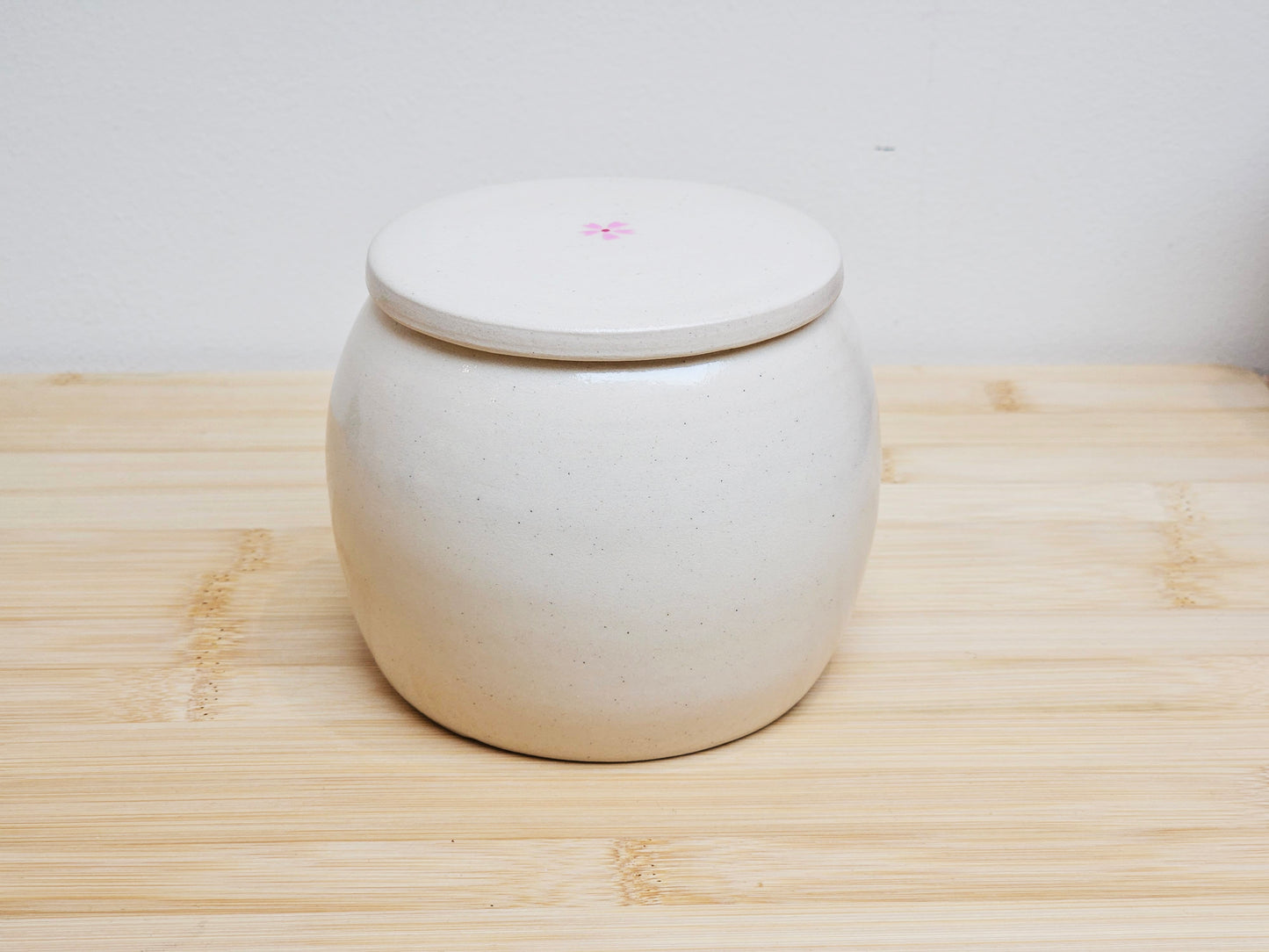 Back view of a handmade ceramic pet urn with a graceful cherry blossom design and scattered petals. The smooth ceramic surface highlights the craftsmanship and natural beauty, making this personalized pet memorial urn a peaceful tribute to a beloved companion.