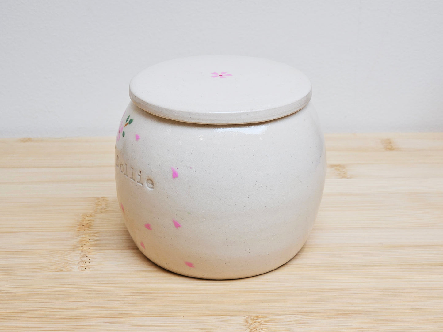 Left side view of a personalised handmade ceramic pet urn, showcasing detailed cherry blossom branches and softly drifting petals. This custom pet memorial urn offers a serene and elegant tribute, perfect for honoring a cherished pet like "Dollie."