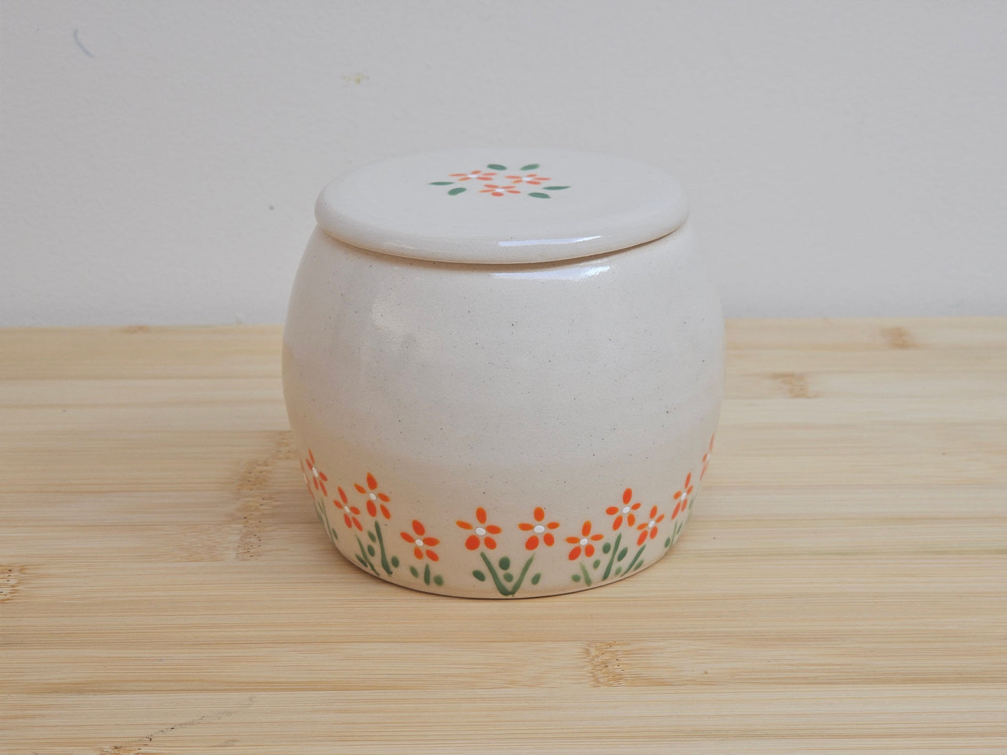 Handmade ceramic pet urn with orange flowers hand-painted around the entire bottom, perfect personalized memorial keepsake for pets.