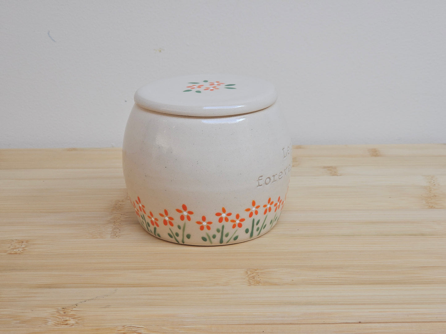 Handmade ceramic pet urn with orange flowers hand-painted around the entire bottom, perfect personalized memorial keepsake for pets.
