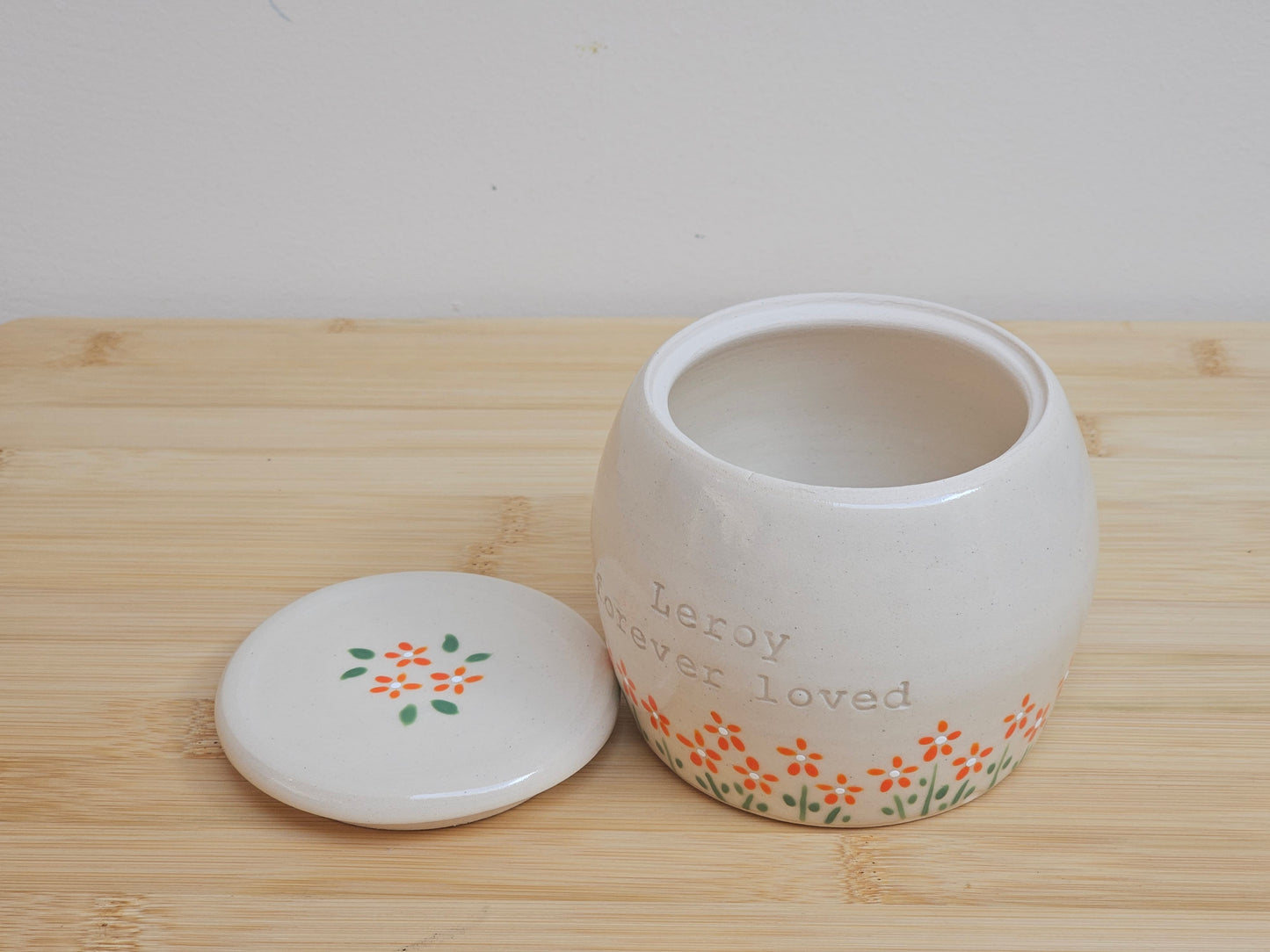 Handmade ceramic pet urn with orange flowers hand-painted around the entire bottom, perfect personalized memorial keepsake for pets.