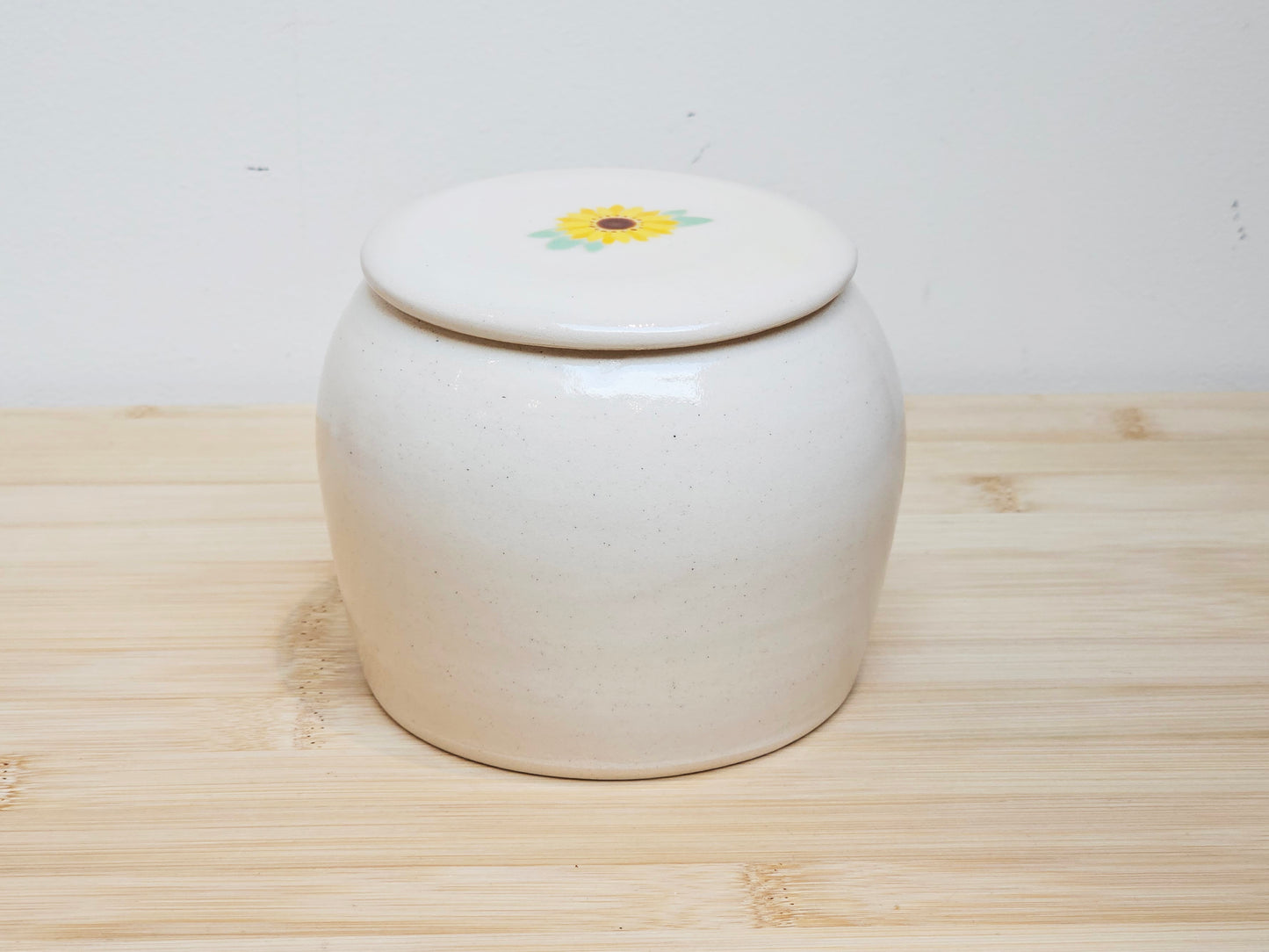 Custom pet urn with a lid featuring a sunflower design on a wooden surface.