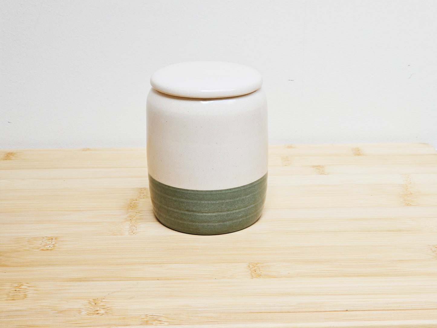 Ceramic container with a white top and green base on a wooden surface