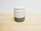 Ceramic container with a white top and green base on a wooden surface