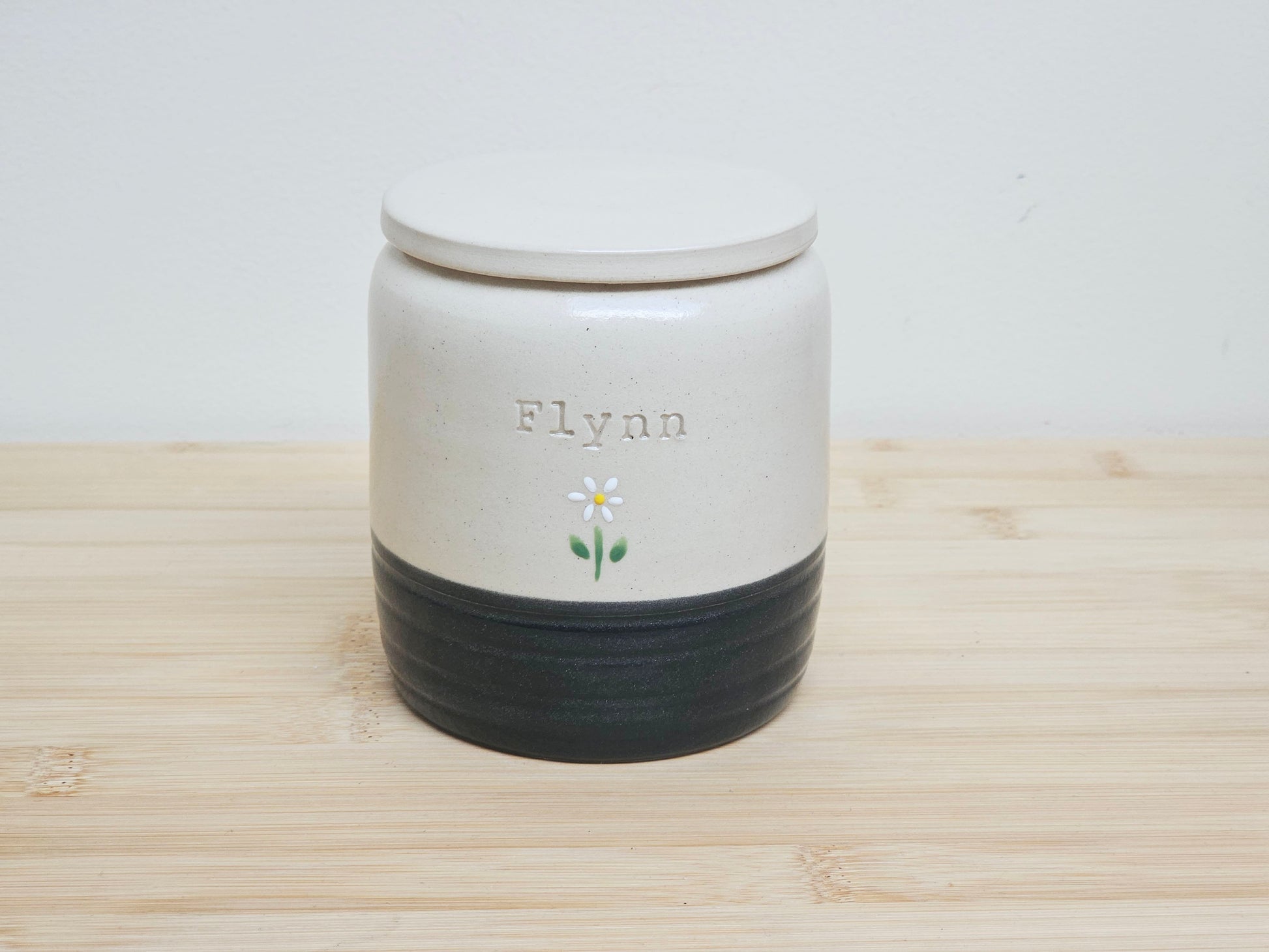 Black pet urn with 'Flynn' and a daisy flower design on a customisable urn. Personalised with name engraved.