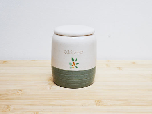 Ceramic urn with 'Oliver' branding on a wooden surface
