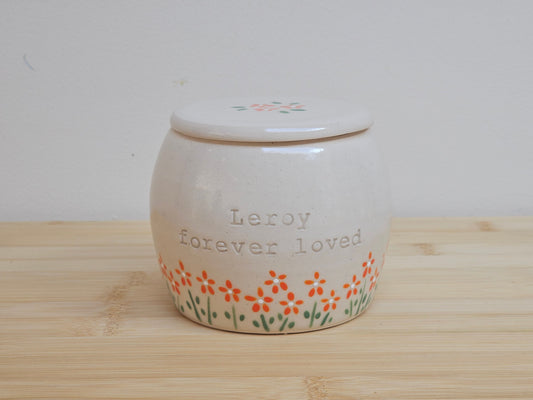 Handmade ceramic pet urn with orange flowers hand-painted around the entire bottom, perfect personalized memorial keepsake for pets.