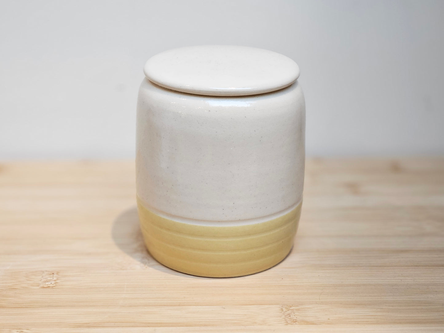 Side profile of custom ceramic pet urn highlighting the contrast between the soft yellow glaze and personalised upper design, handmade in the UK studio.