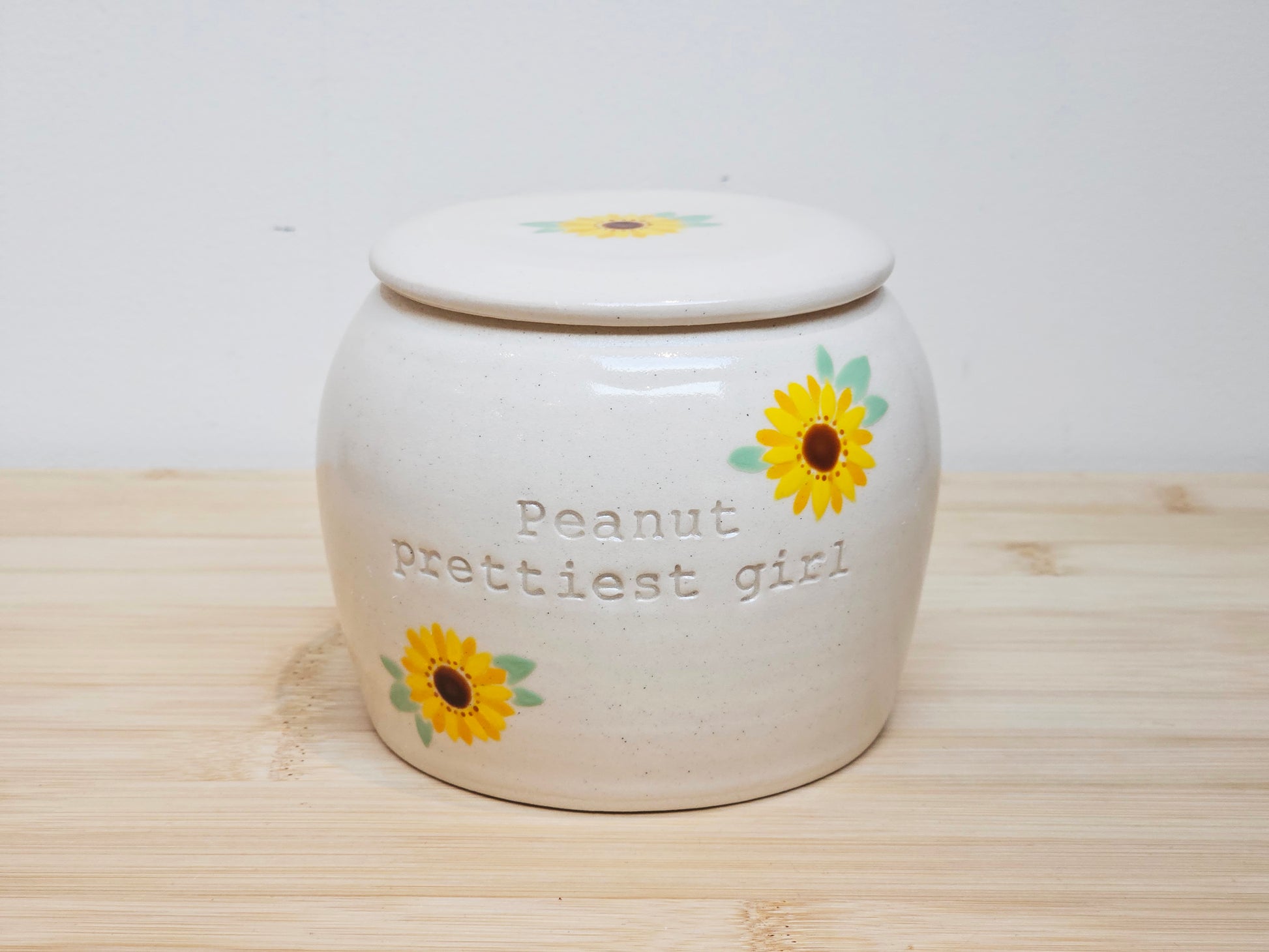 White ceramic jar with sunflower designs and text on a wooden surface