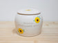 White ceramic jar with sunflower designs and text on a wooden surface