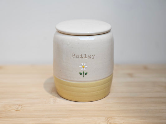 Handmade ceramic pet urn with soft yellow glazed base and hand-painted floral design on the upper half, displayed on a neutral background.