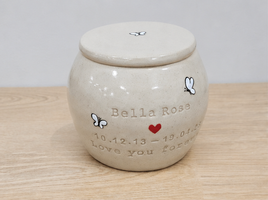 Ceramic urn with 'Bella Rose' and personalized text on a wooden surface