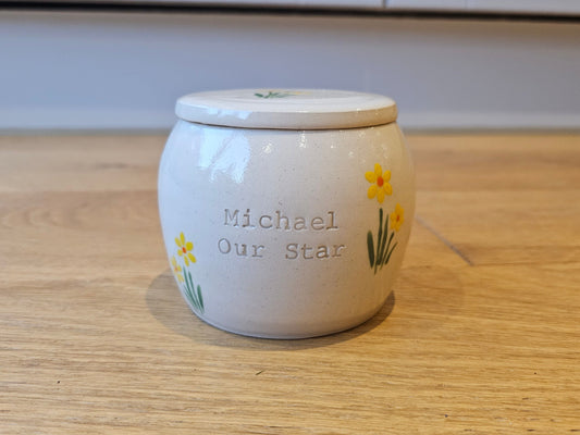 Handmade ceramic pet urn featuring a delicate hand-painted daffodil design, perfect for honouring your beloved pet. This personalised dog urn is ideal for pet cremation, offering a secure and elegant resting place for ashes. Suitable for both canine urns and feline urns, it can be customised with name engraving, making it a meaningful keepsake for dogs or cats. This custom pet urn doubles as an ashes box for pets, a burial box for dogs, or a memorial box for dogs. Perfect for those seeking engraved dog urns