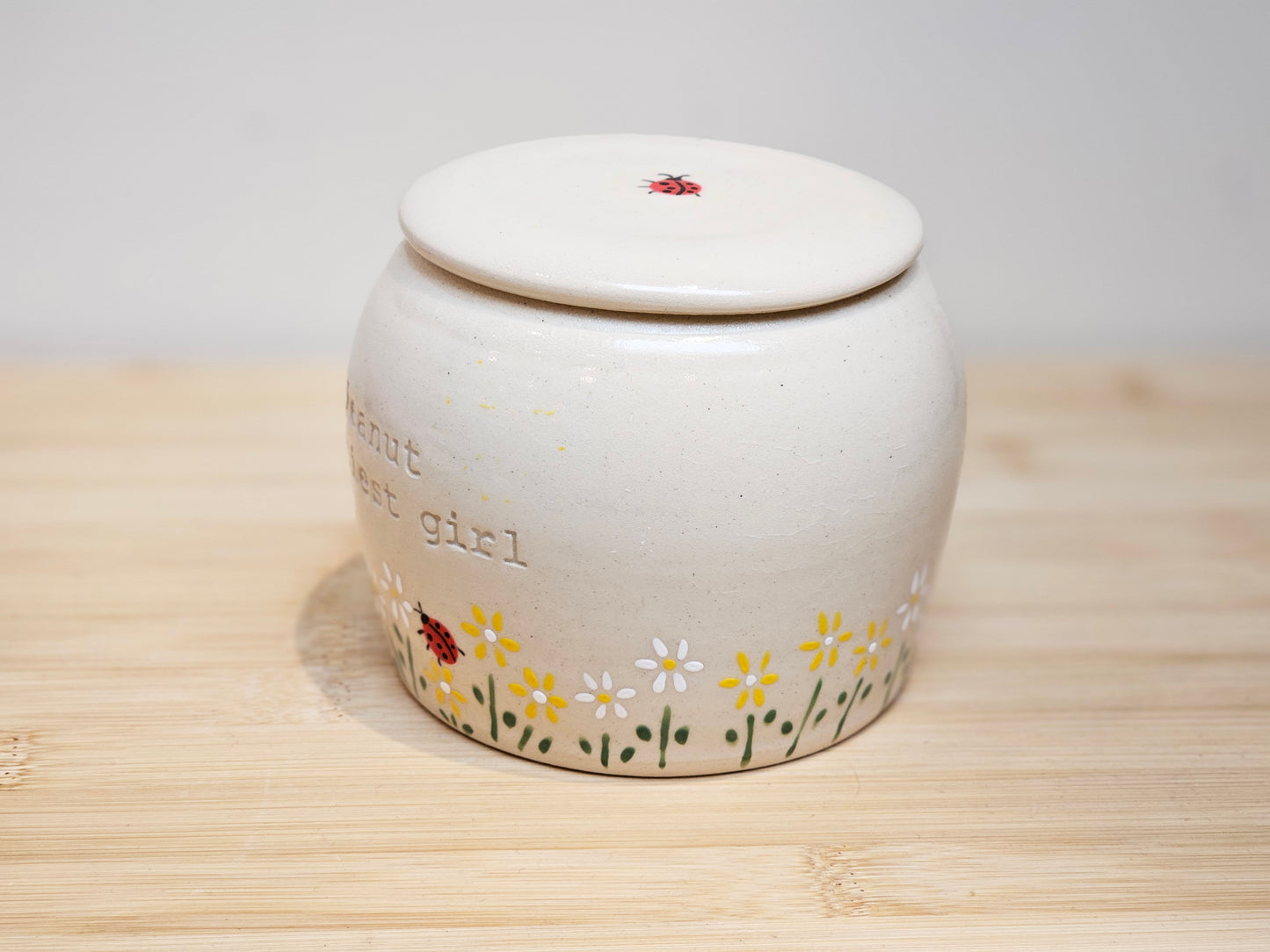 White ceramic jar with floral designs and text on a wooden surface