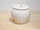 White ceramic jar with floral designs and text on a wooden surface