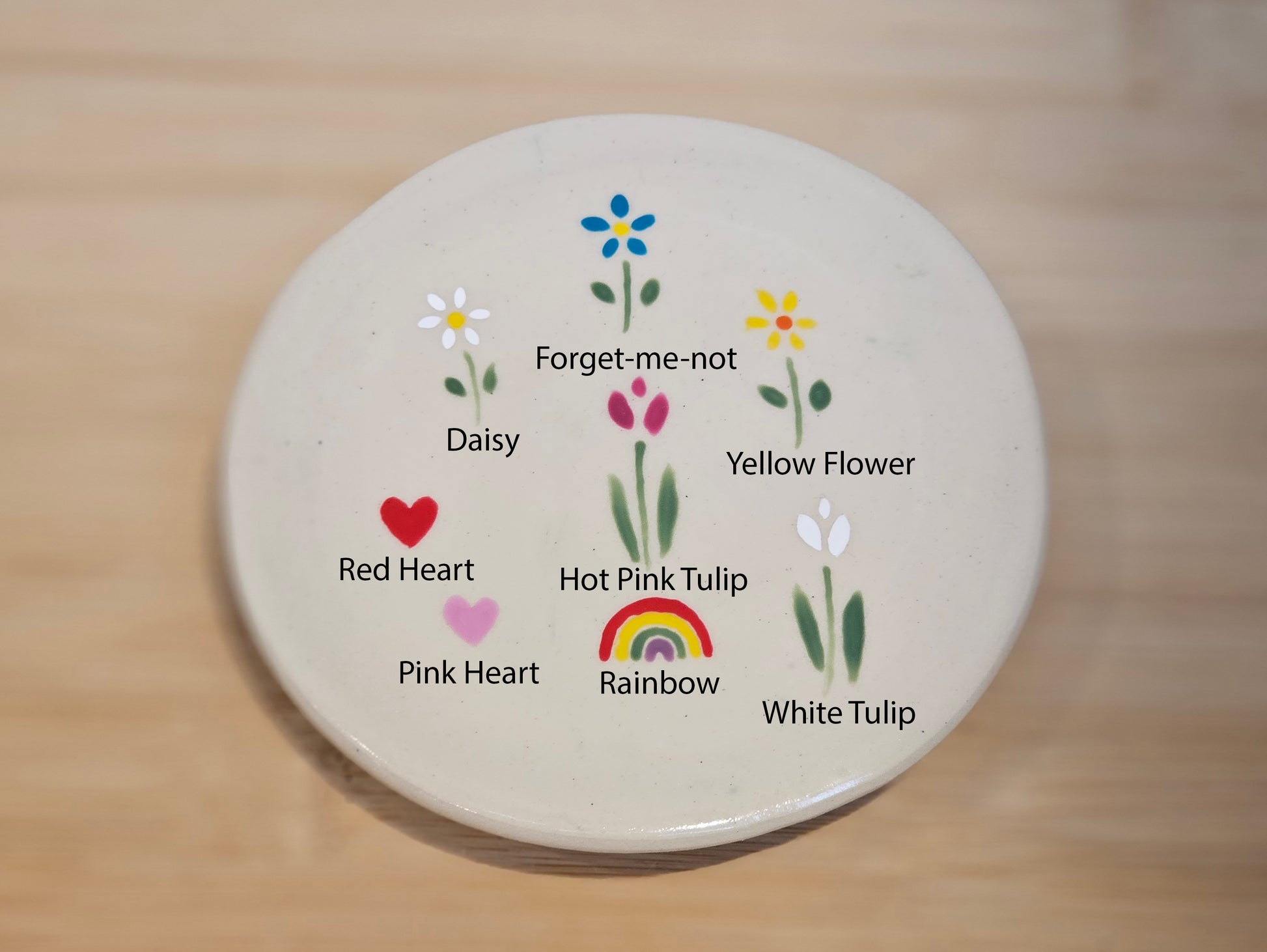 Round ceramic coaster with floral and heart designs on a wooden surface