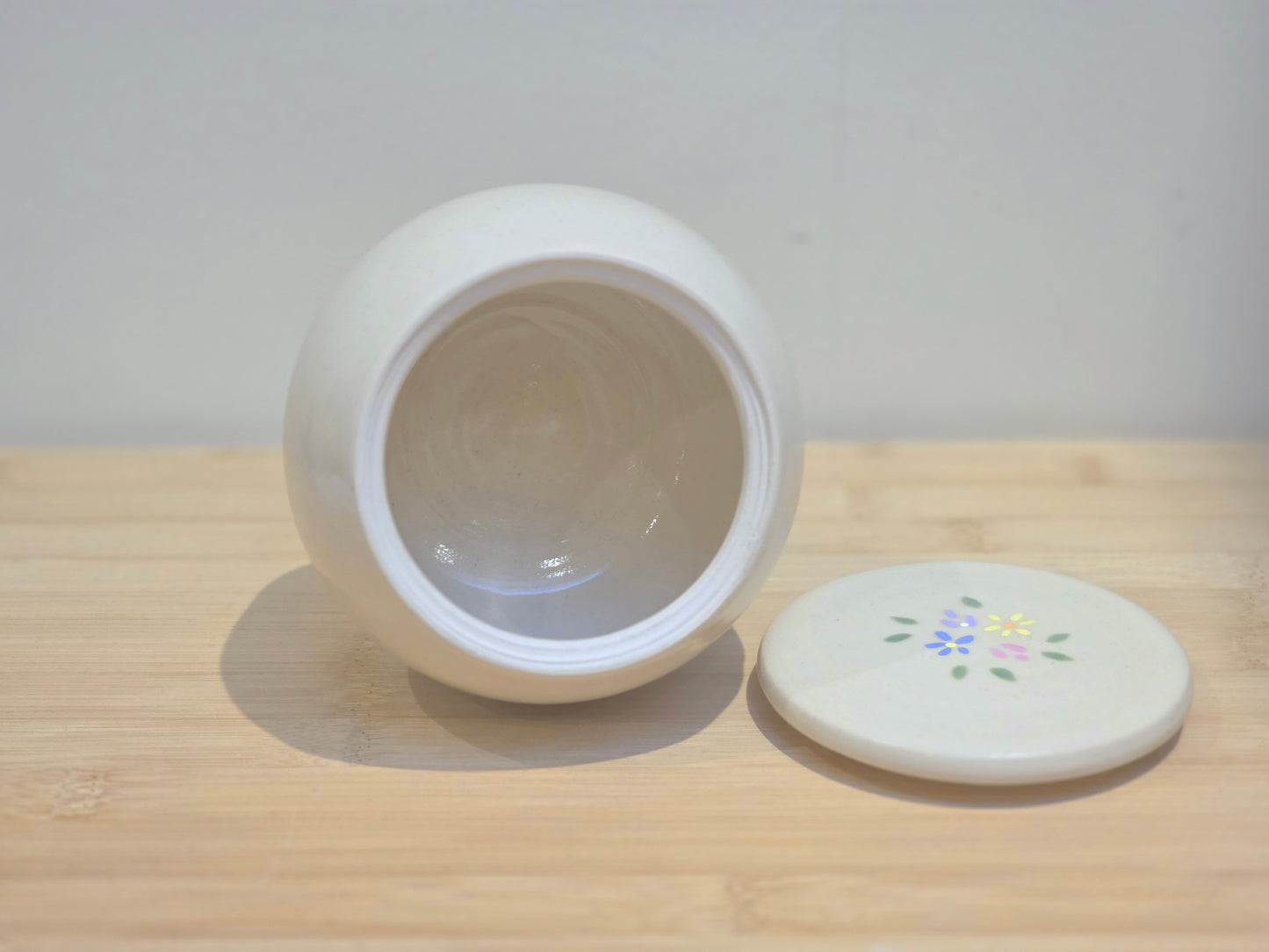 White ceramic urn with a lid on a wooden surface