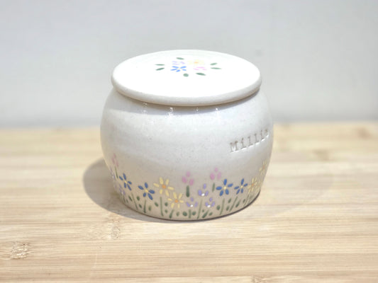 White ceramic jar with floral designs on a wooden surface