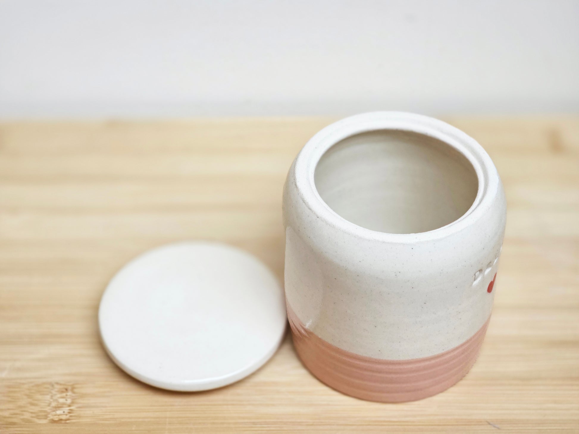 White ceramic container with a pink base on a wooden surface, lid off.
