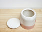 White ceramic container with a pink base on a wooden surface, lid off.