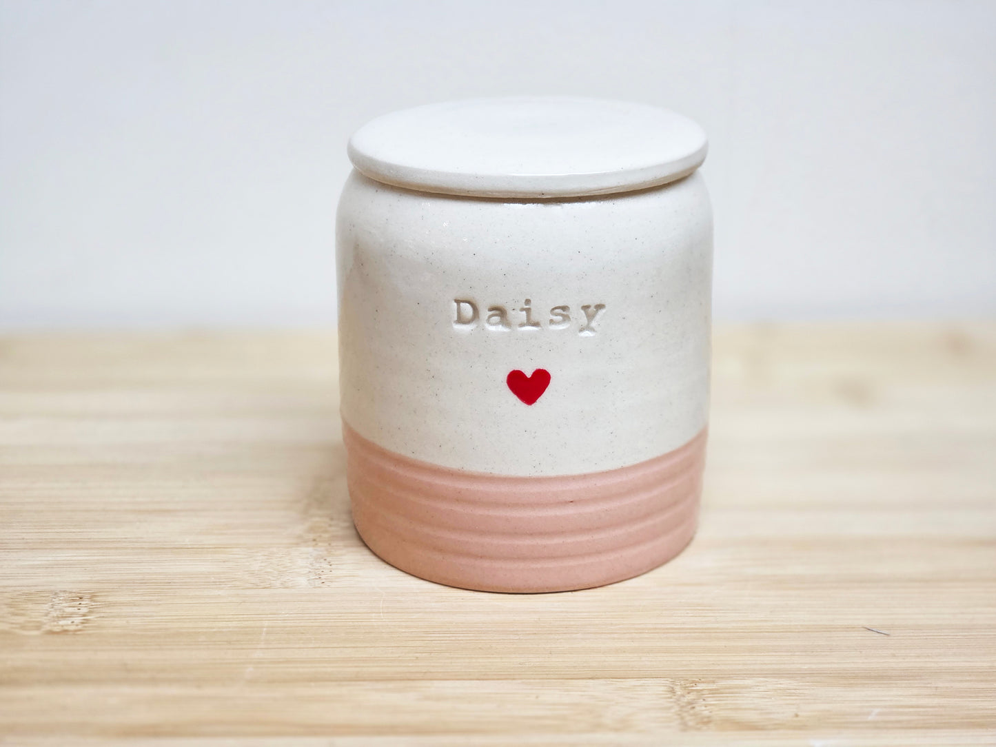 Ceramic jar in cream and pink, with 'Daisy'  stamped on the side and a heart on a wooden surface