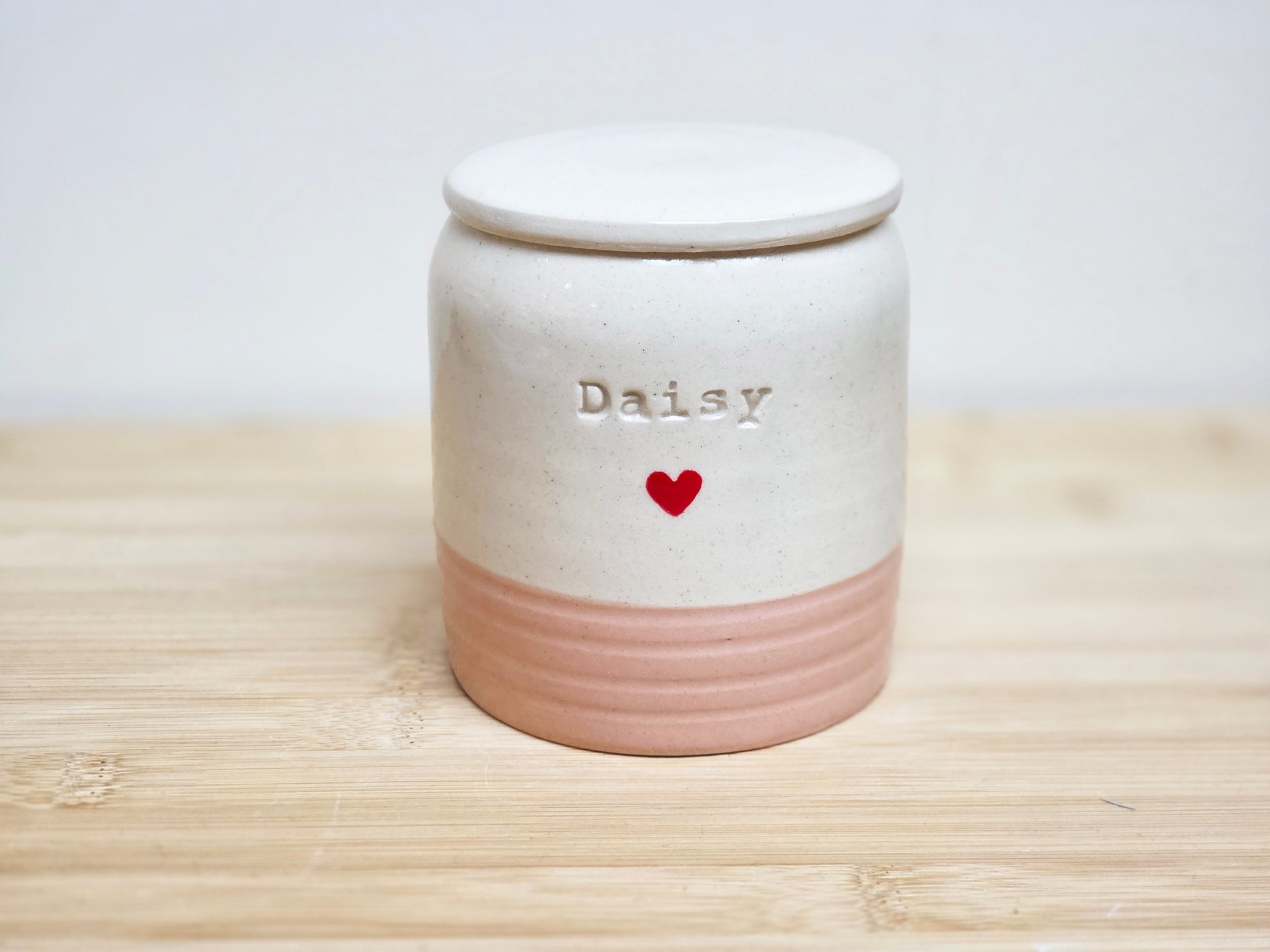 Ceramic jar in cream and pink, with 'Daisy'  stamped on the side and a heart on a wooden surface
