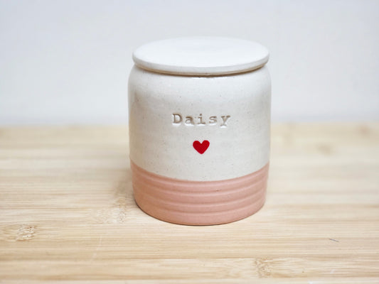 Ceramic jar in cream and pink, with 'Daisy'  stamped on the side and a heart on a wooden surface