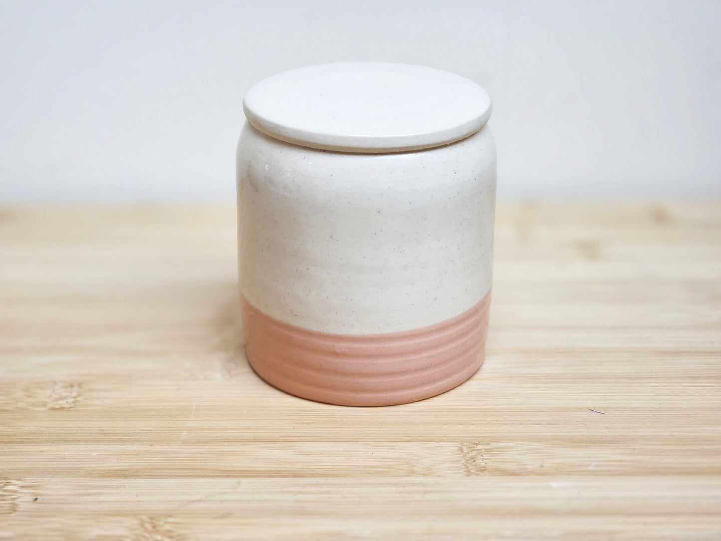 Ceramic jar with a white lid and pink base on a wooden surface