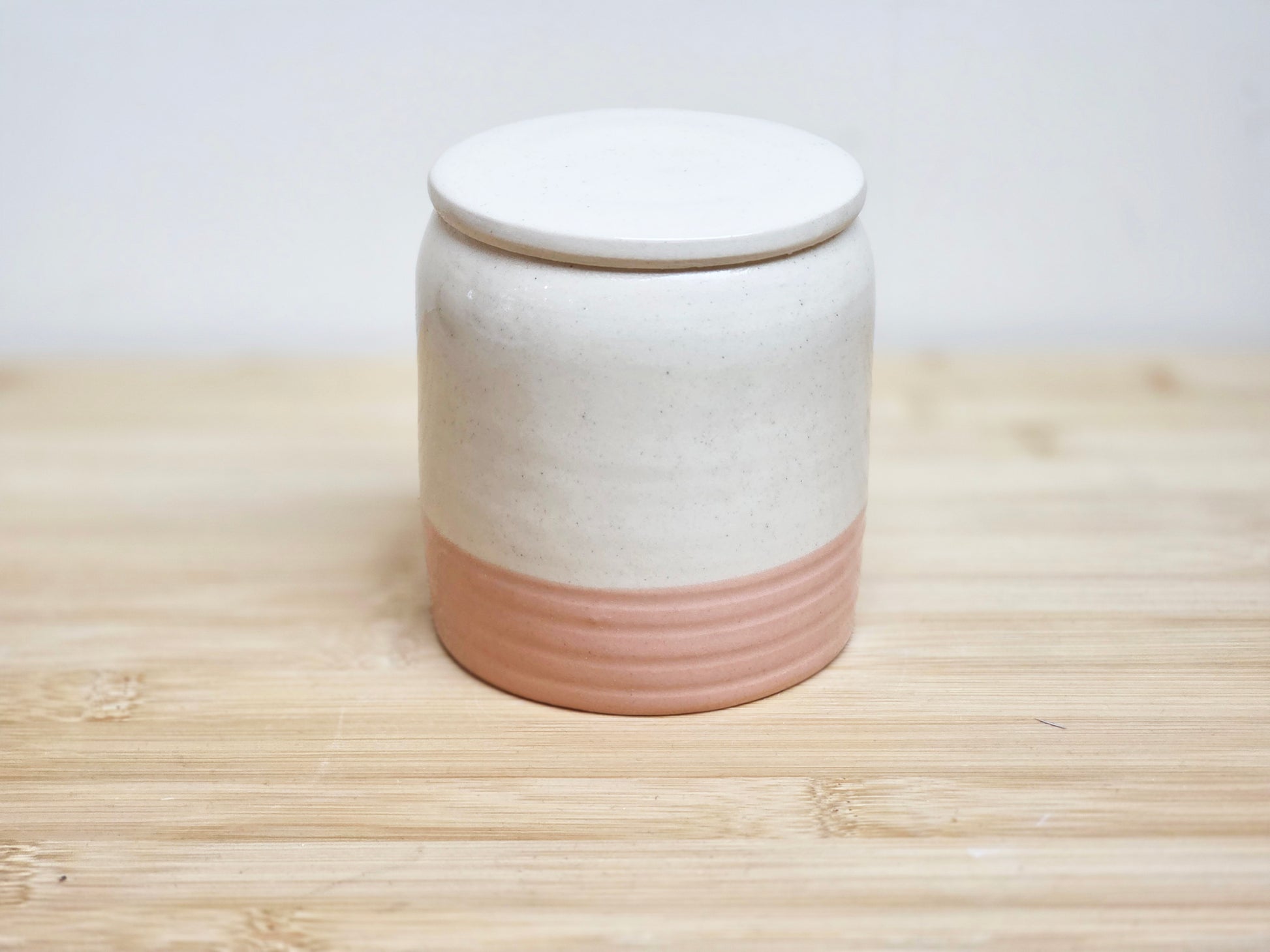 Ceramic jar with a white lid and pink base on a wooden surface