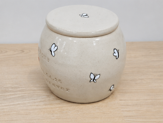 White ceramic urn with white butterfly designs and text on a wooden surface