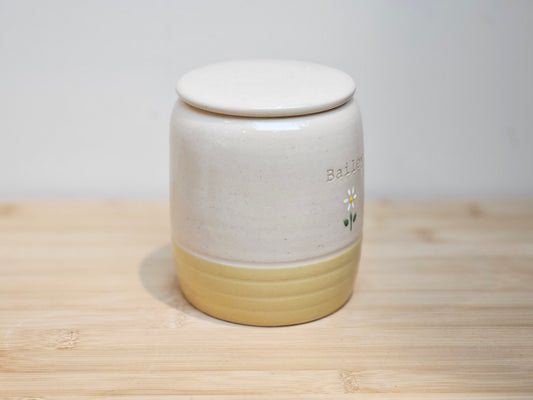 Close-up of personalised ceramic pet urn showing calming yellow glaze and hand-decorated daisy motif.